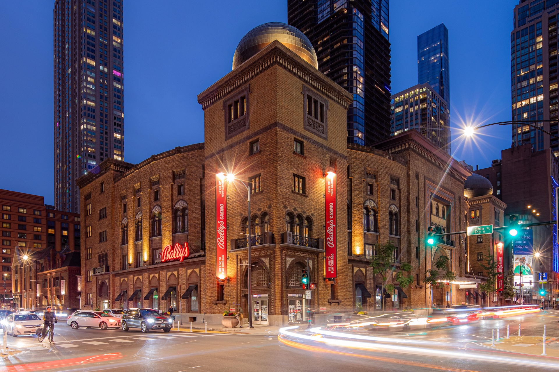 A brick building with a dome on top is shown at night with city lights and traffic.