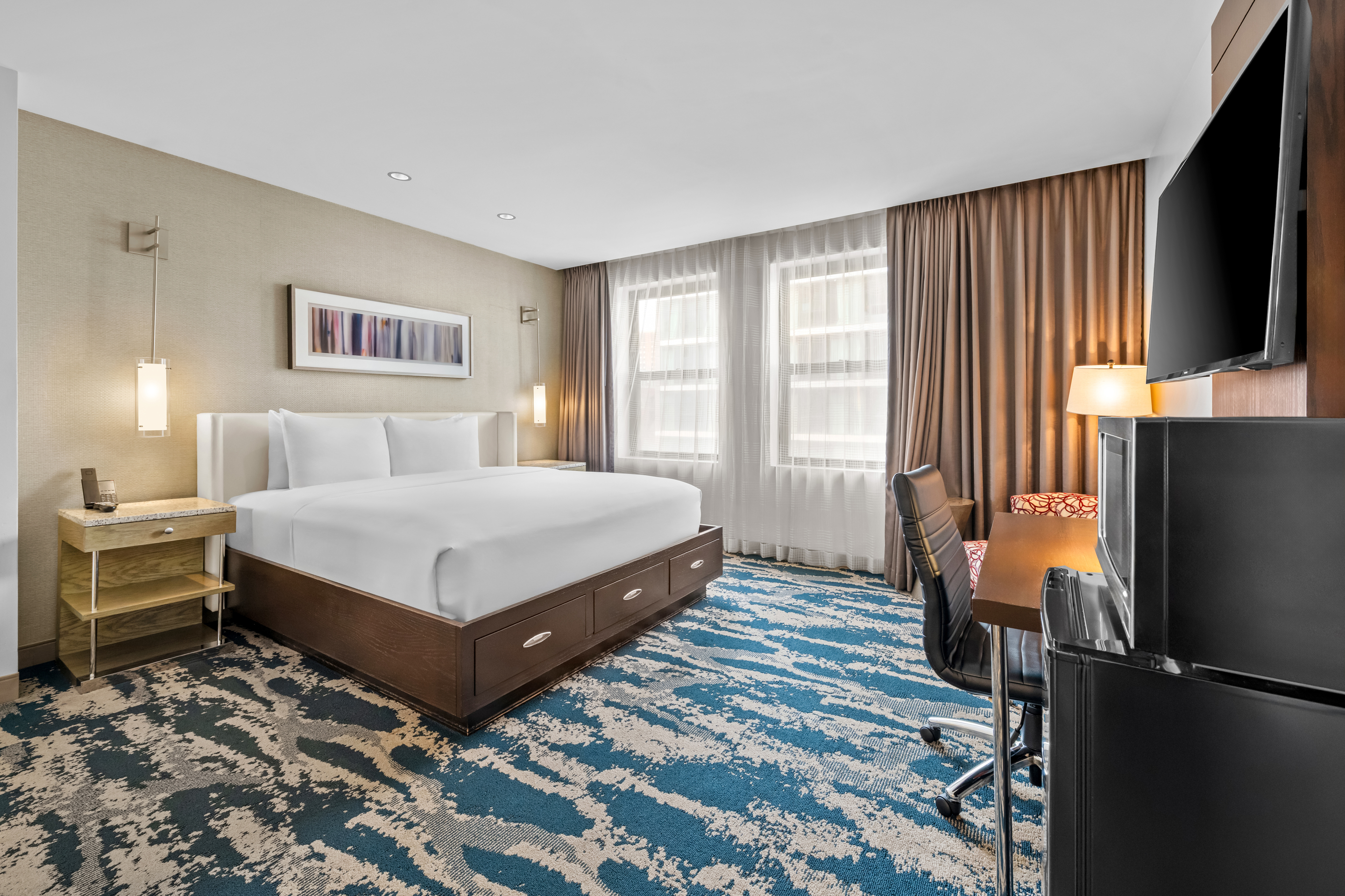 A wide view of a hotel room with a bed, desk, TV, and window