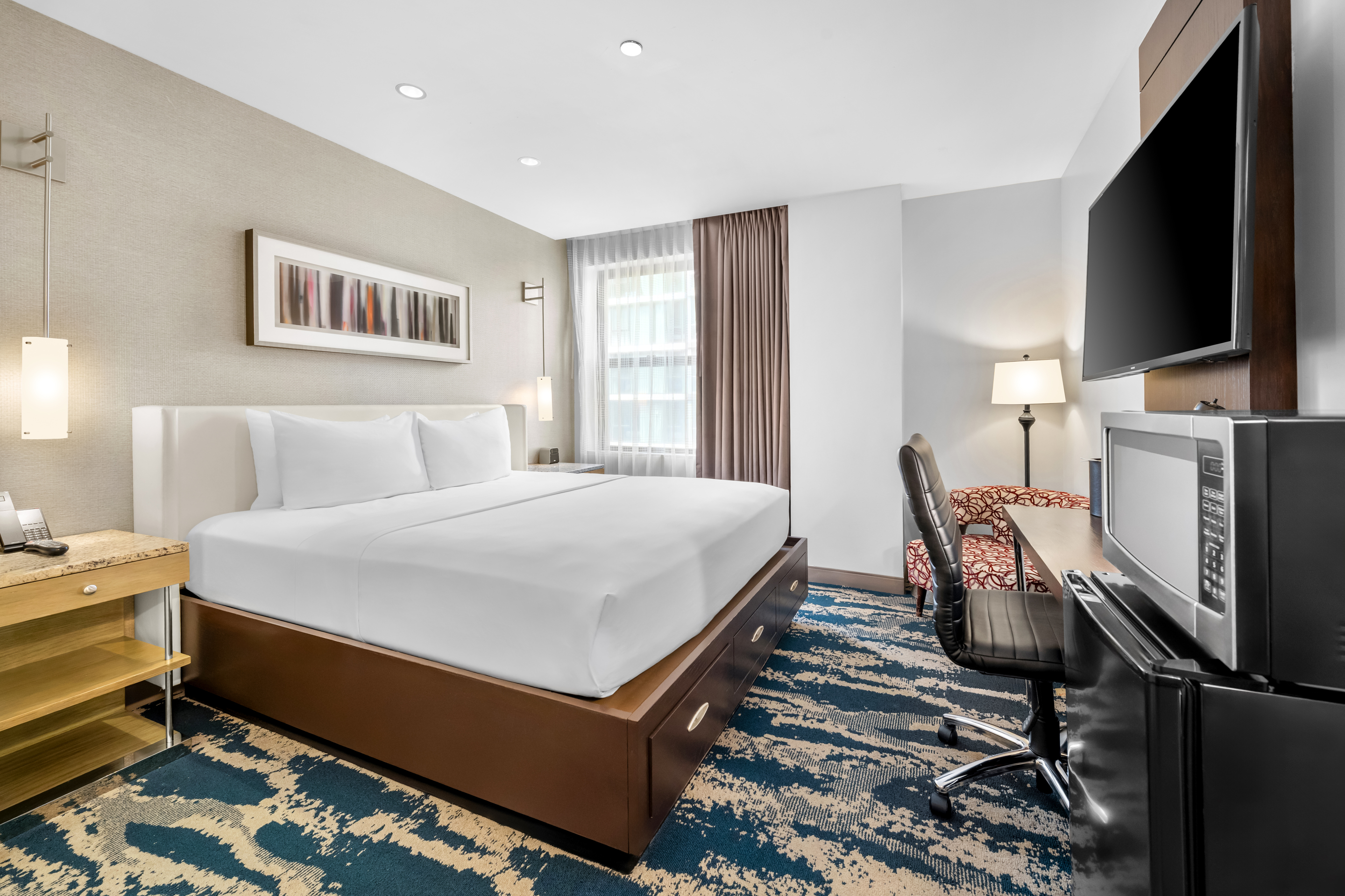 A wide view of a hotel room with a king-sized bed, desk, TV, and window