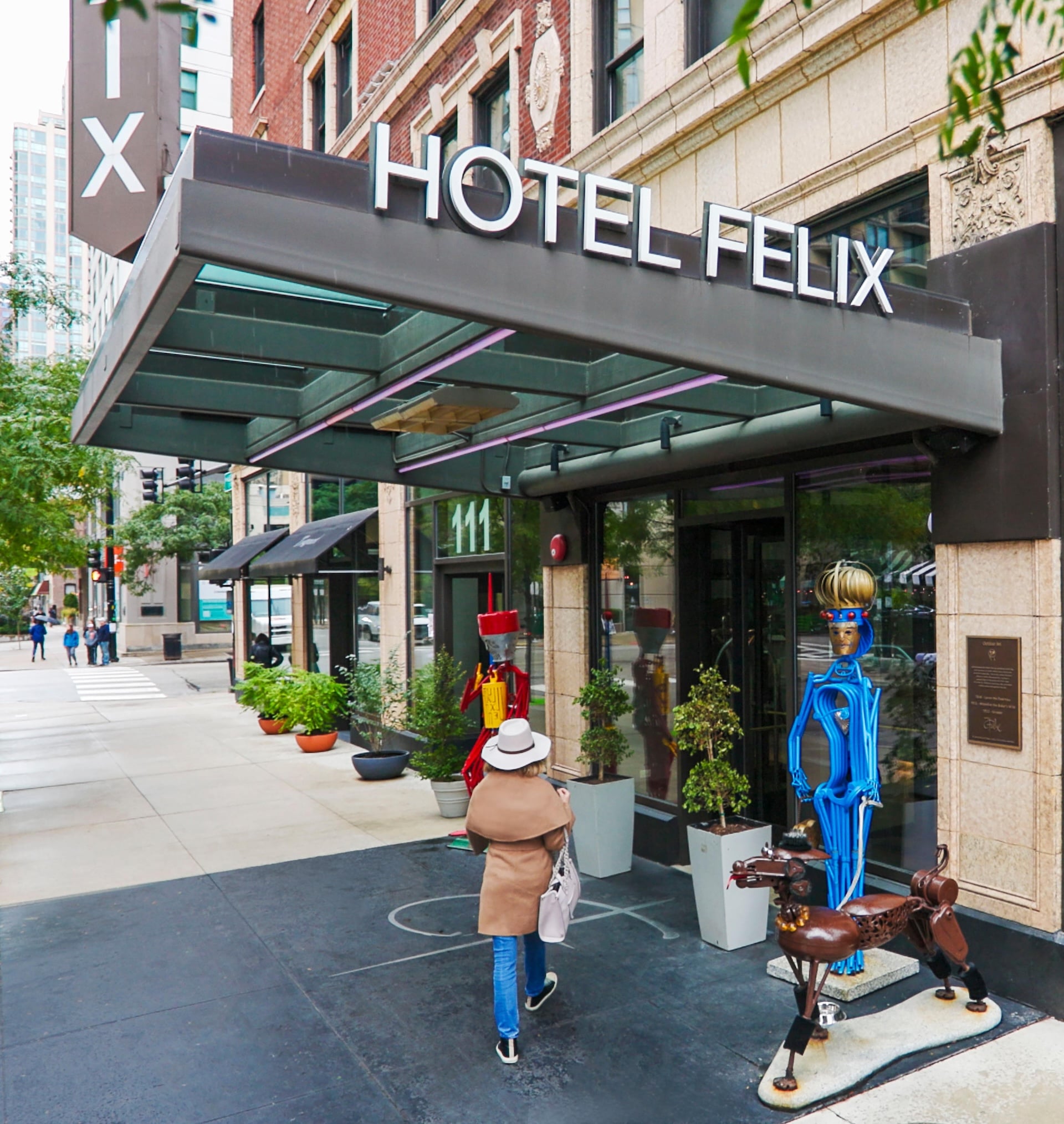 The exterior of a hotel with a glass awning and a statue in front of it.
