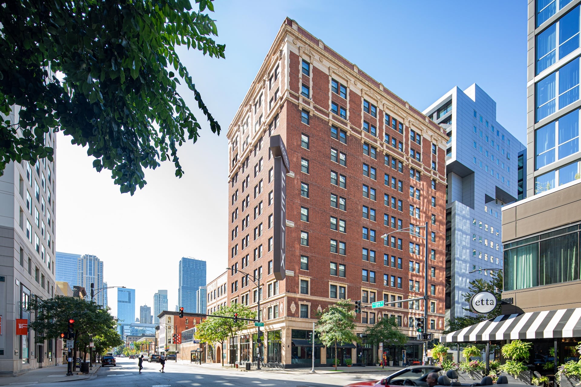A red brick building with many windows stands on a city street corner.
