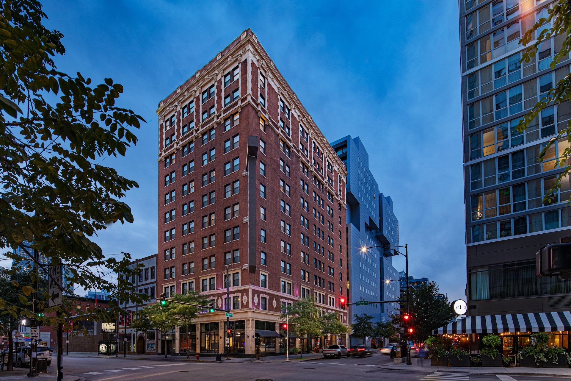 A red brick hotel building with multiple stories stands on a street corner in an urban setting.