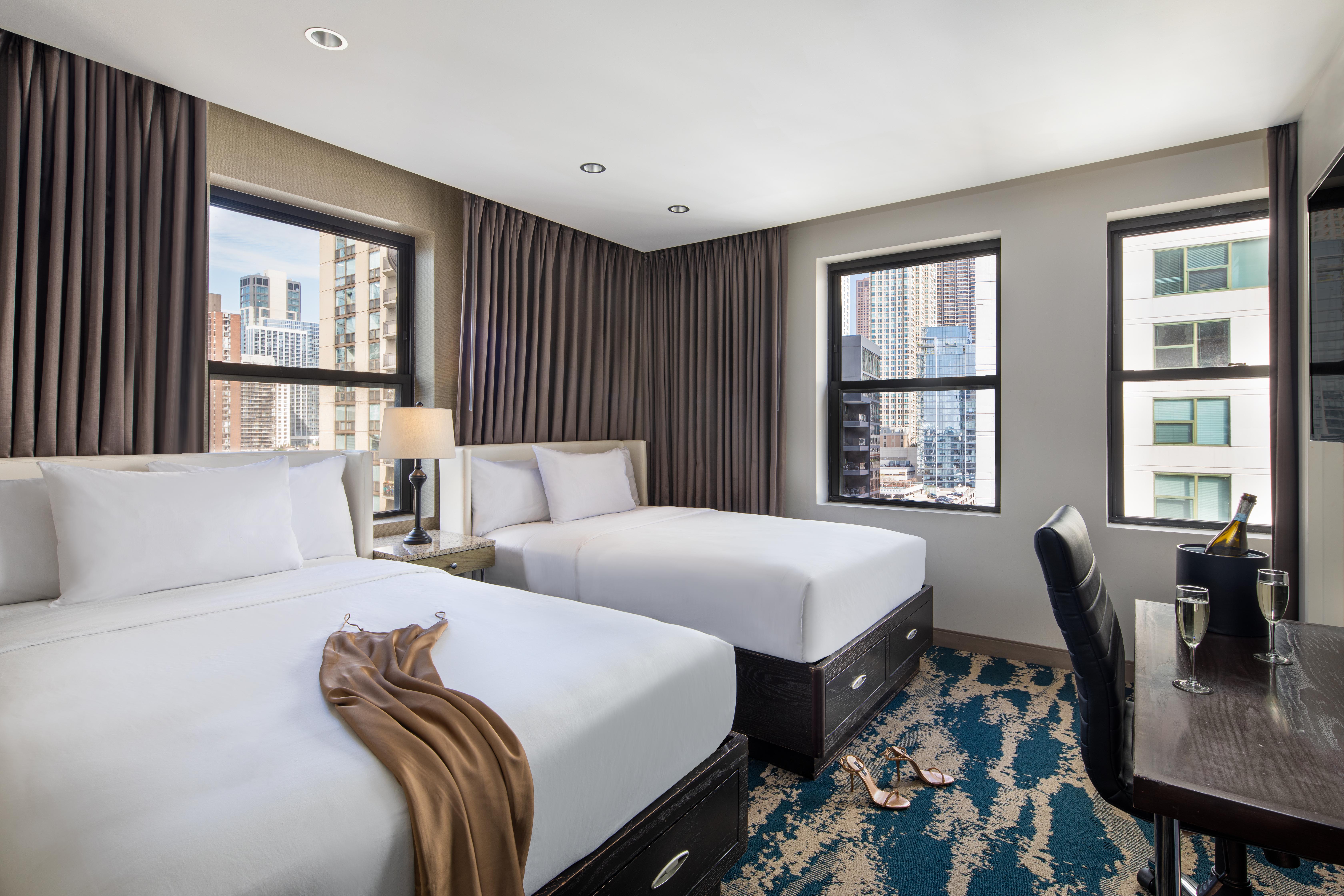 A hotel room with two beds, a desk, and a city view