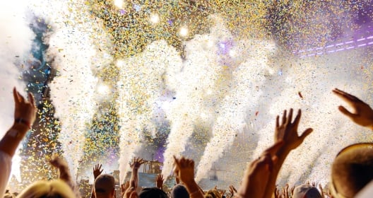 People Cheering and Dancing under Confetti at Music Festival with intense Light Show