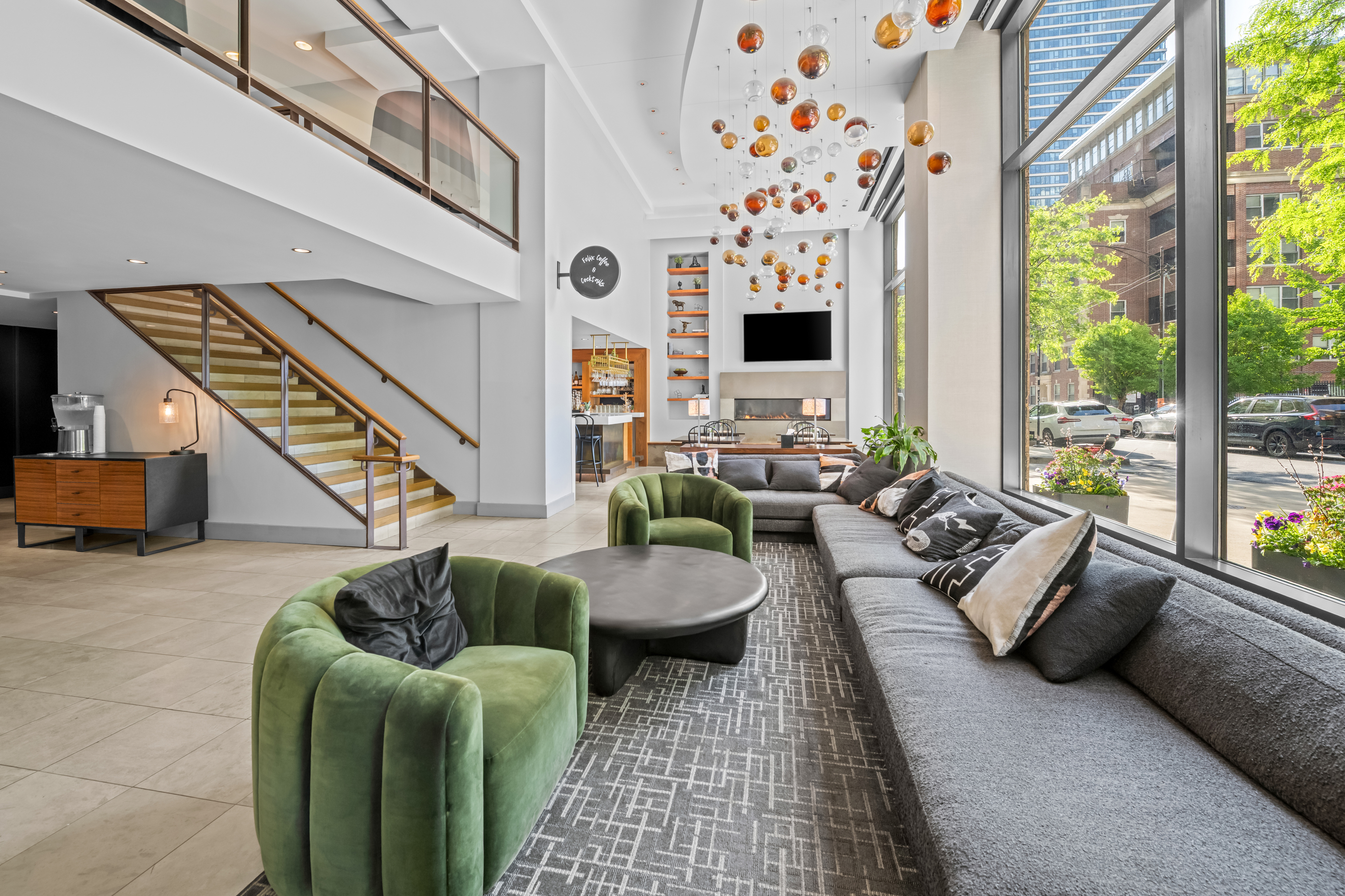 A spacious hotel lobby with a staircase, seating area, and large windows